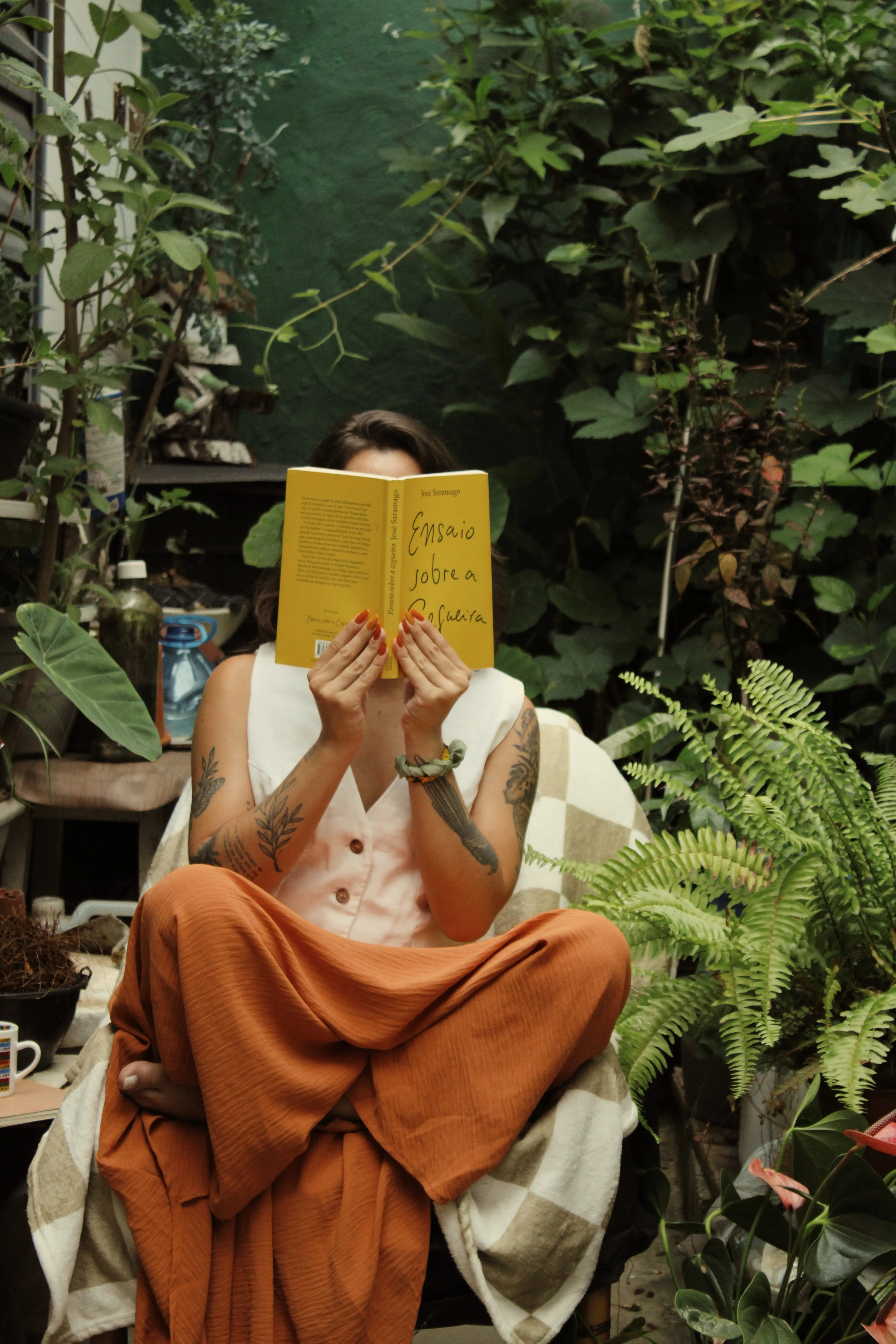 Pessoa lendo um livro amarelo em meio a plantas